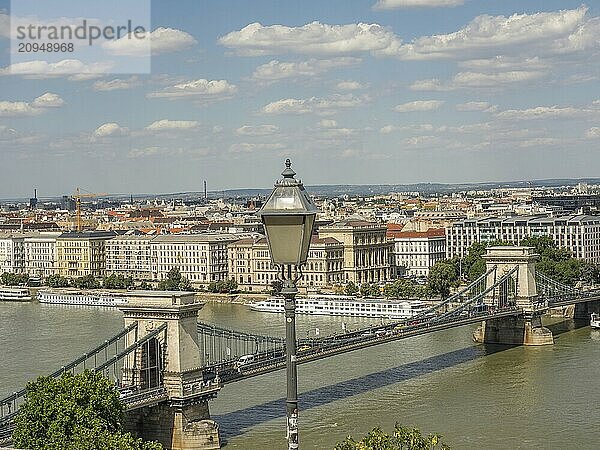 Stadtansicht mit Fokus auf eine Straßenlaterne  eine Brücke über einen Fluss und viele Gebäude unter einem bewölkten Himmel  budapest  donau  ungarn