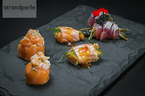 Sushi  traditionelle japanische Küche. Mehrere köstliche Sushi auf dem dekorierten Teller  schwarzer Hintergrund. Gruppe von Sushi  Urakami  Nigori  Sushi jow  Sashimi  Tekamaki  etc