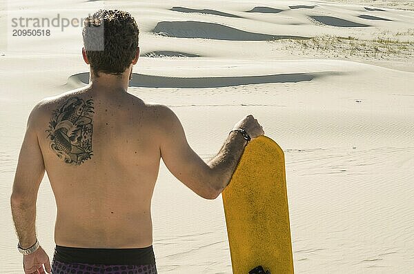 Junger Mann auf dem Rücken mit Blick auf die Sanddünen  Vorbereitung auf das Sandboarding