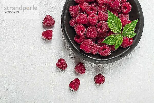 Frische Himbeeren  auf einem schwarzen Teller  mit Blättern  Draufsicht  auf einem weißen Tisch