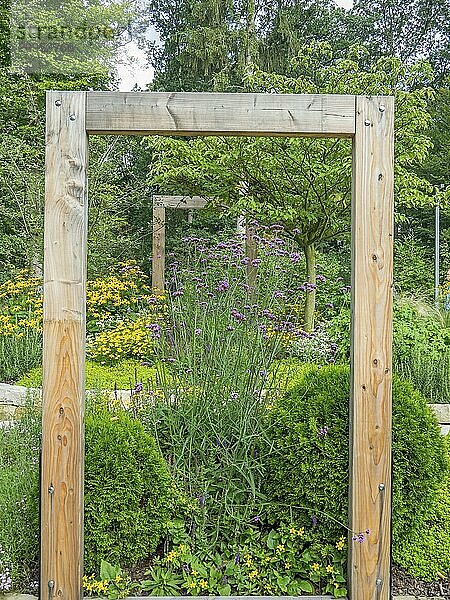 Gartenansicht durch einen dekorativen Holzrahmen mit blühenden Blumen und grünem Laub  Schloss Neuhaus  Deutschland  Europa