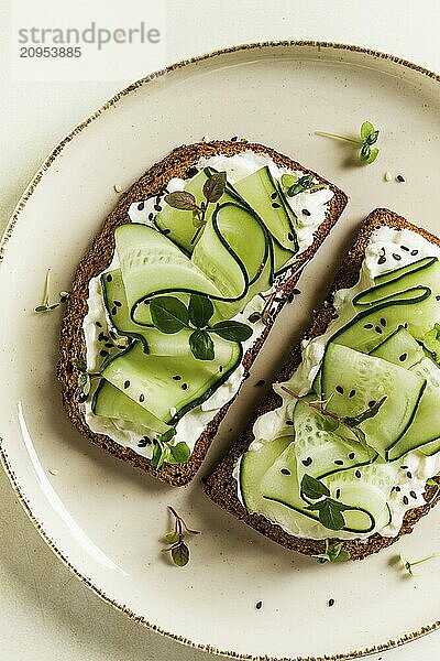 Frühstück  Müslibrötchen  Frischkäse  Gurkenscheiben  mit Mikrogrün auf einem hellen Tisch  Nahaufnahme  Draufsicht  selektiver Fokus  keine Personen