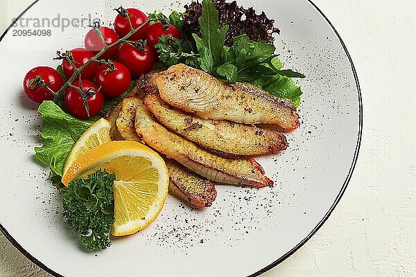 Gebratenes Tilapia Fischfilet  in Gewürzen  mit Kirsche und Salat  auf einem weißen Teller  hausgemacht  ohne Personen