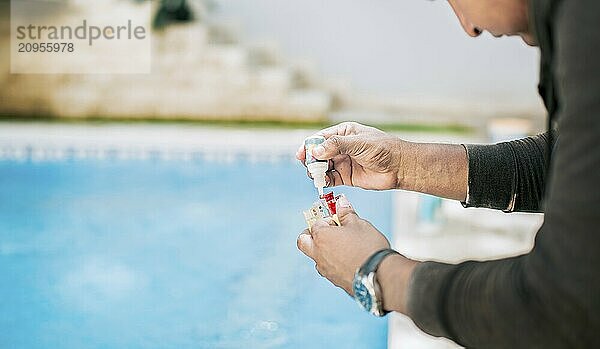 Mann mit Testgerät zur Messung von Chlor und pH Wert im Schwimmbad. Person  die den PH Wert des Schwimmbads testet