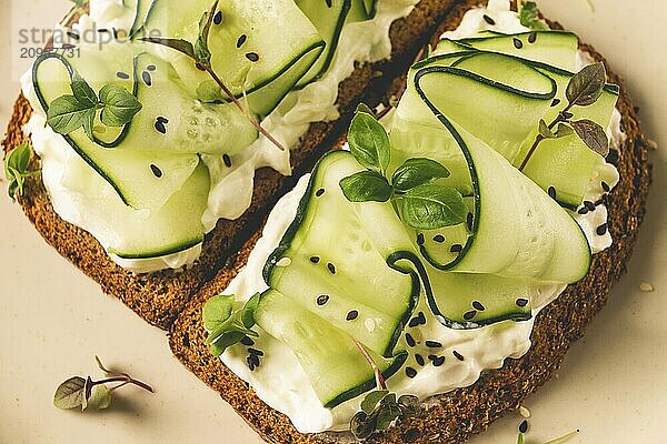 Frühstück  Müslibrötchen  Frischkäse  Gurkenscheiben  mit Mikrogrün auf einem hellen Tisch  Nahaufnahme  Draufsicht  selektiver Fokus  keine Personen