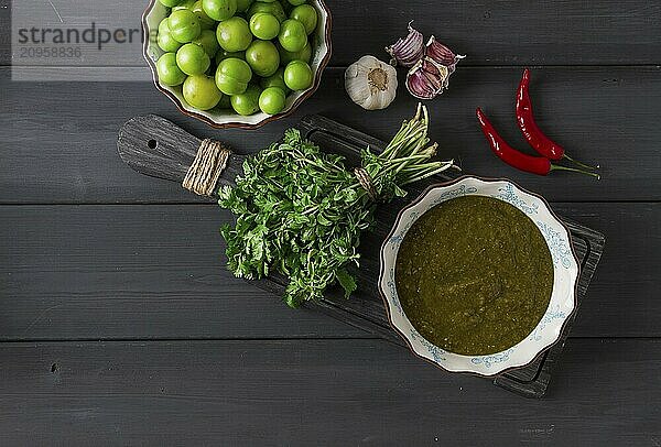 Tkemali Sauce  traditionelle georgische Küche  grüne Kirschpflaume  mit Zutaten für die Sauce  Koriander  Minze  scharfer Pfeffer  Knoblauch  auf einem Holztisch  Nahaufnahme  rustikal  Lebensmittel Hintergrund  keine Menschen  selektiver Fokus  Sauce  grüne Sauce  tkemali  georgische Küche  hausgemacht