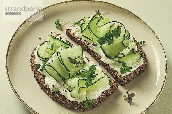 Frühstück  Müslibrötchen  Frischkäse  Gurkenscheiben  mit Mikrogrün auf einem hellen Tisch  Nahaufnahme  Draufsicht  selektiver Fokus  keine Personen