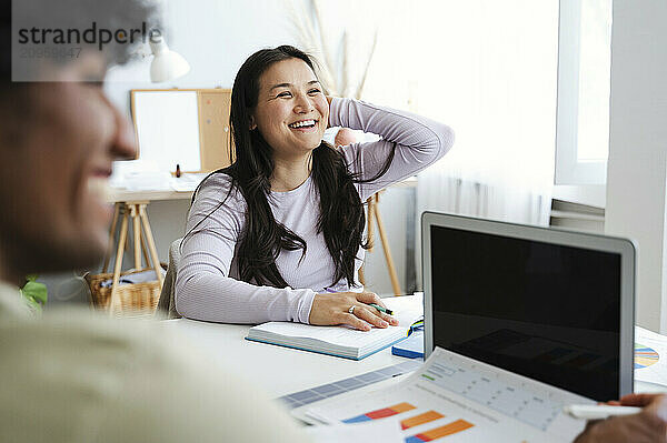 Happy woman with hand in hair studying with friend at home