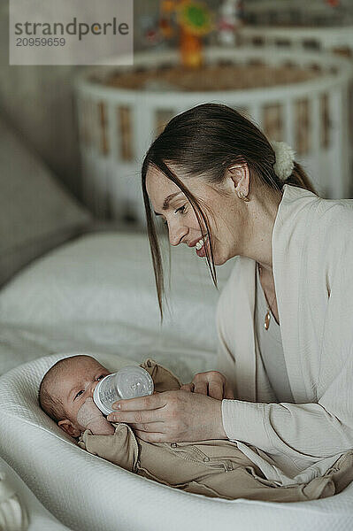 Mother feeding baby boy lying in cocoon cradle at home