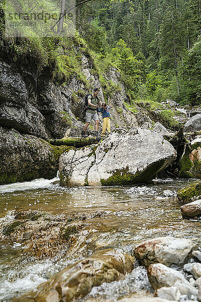 Father and daughter hiking on rocks near river stream in forest