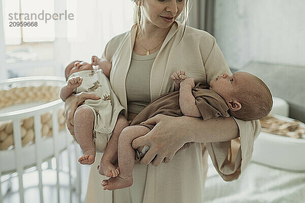 Mother carrying newborn twins and standing at home