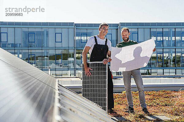 Craftsman and colleague installing solar panel on company building roof  contributing to sustainable energy practices