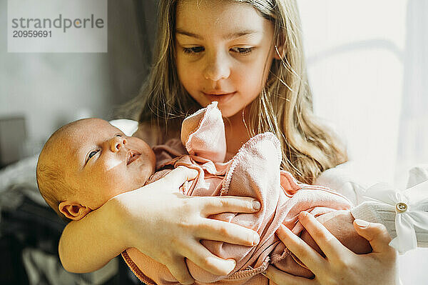 Girl holding newborn baby in arms at home