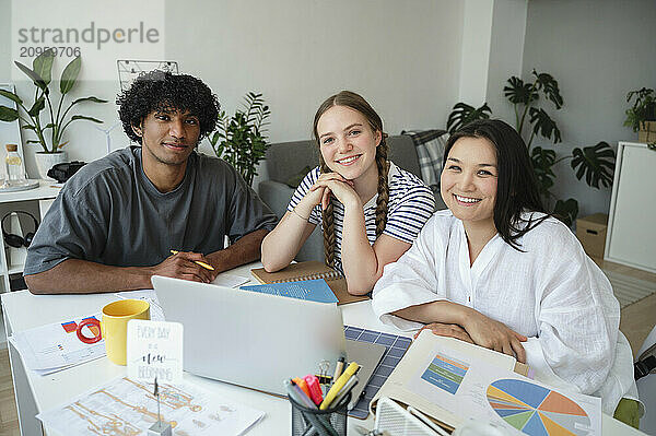 Smiling multiracial friends sitting near table at home