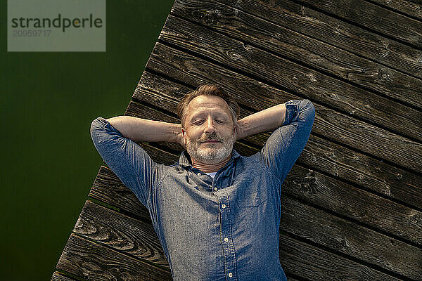 Carefree man with eyes closed lying on pier near lake