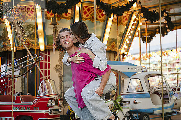 Boyfriend giving piggyback ride to girlfriend in front of carousel