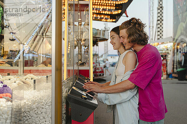 Cheerful couple playing toy grabbing game in amusement park