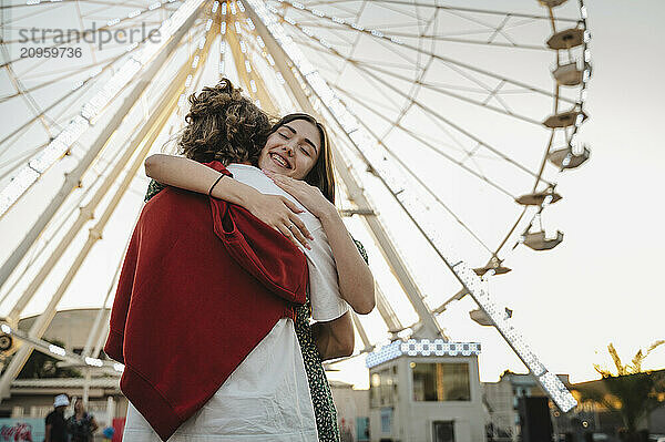 Girlfriend embracing boyfriend in front of ferris wheel at park