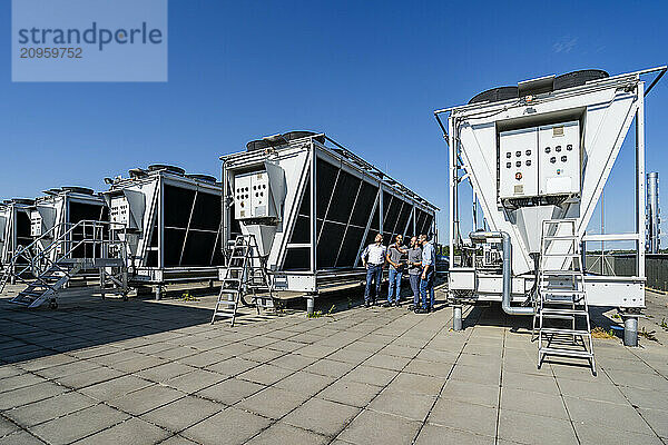 Businessmen and employees having a meeting on rooftop beside refrigeration installation