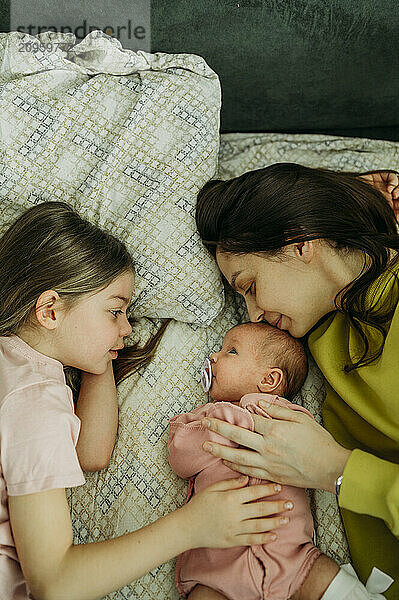 Mother and sister lying with baby girl on bed