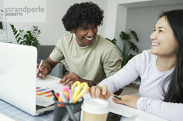 Happy curly haired man doing project with friend at home