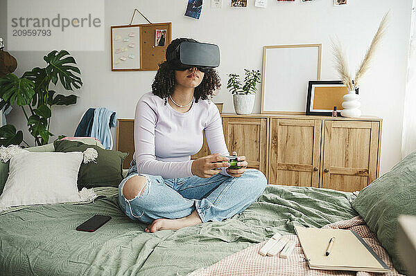 Girl wearing virtual reality simulators holding game controller on bed at home