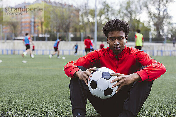 Soccer player sitting with ball on field