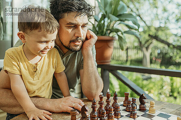 Father and son spending leisure time playing chess sitting on porch