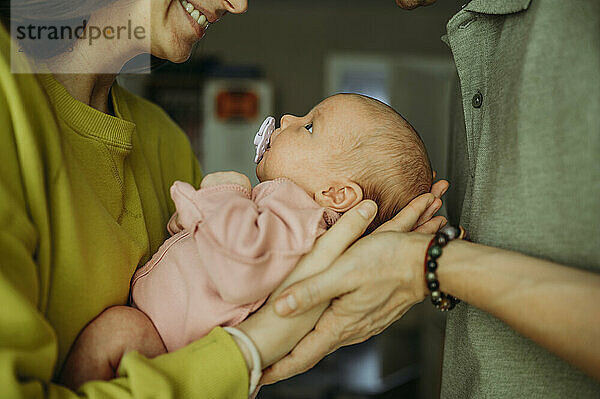 Parents carrying newborn baby sucking pacifier at home