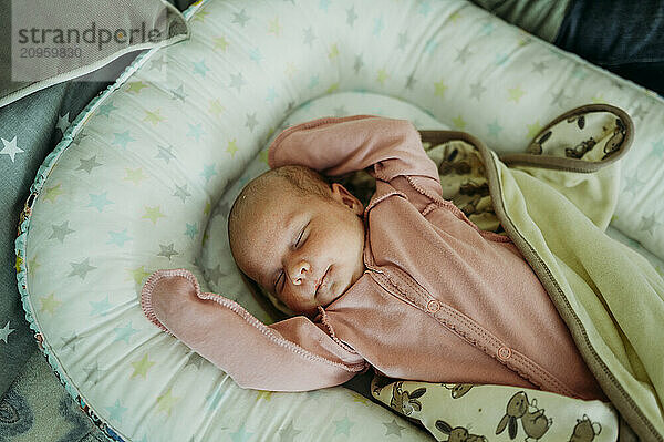 Cute baby girl sleeping with arms raised in bed