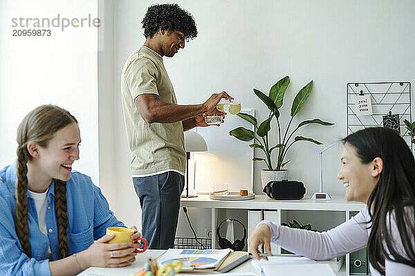 Young man pouring water with friends discussing near table at home