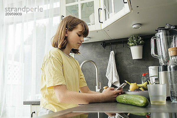 Girl leaning on kitchen counter and using smart phone at home