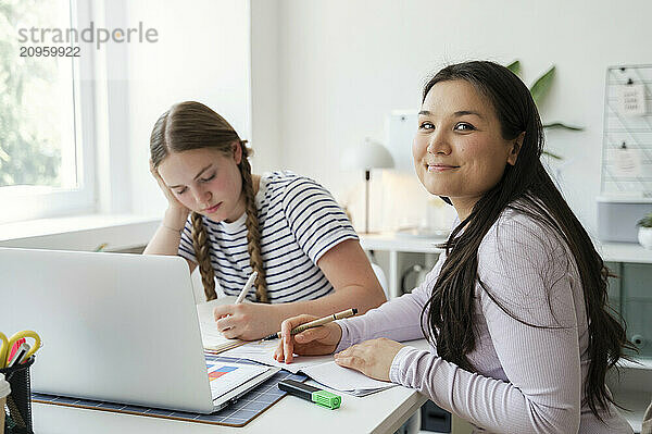 Smiling woman doing homework with friend at home