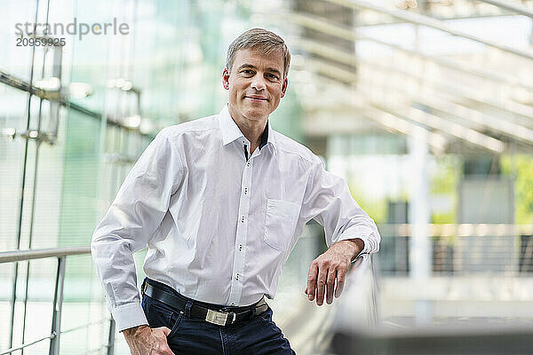 Confident businessman leaning on railing in office building