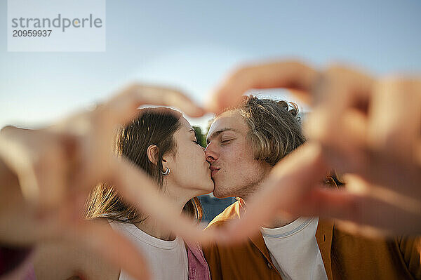 Couple kissing and making heart symbol with hands