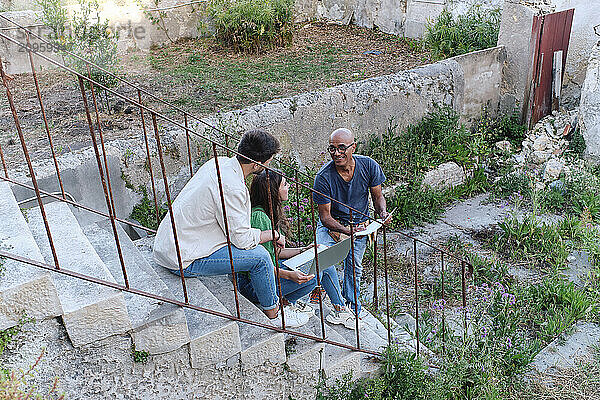 Happy mature architect explaining plan over document to couple at site