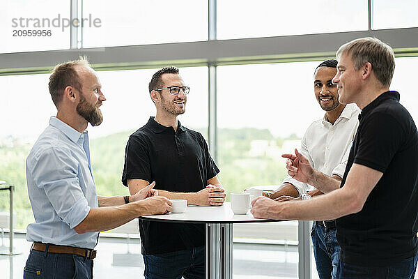 Group of businessman having informal meeting standing in office hall with cups of coffee