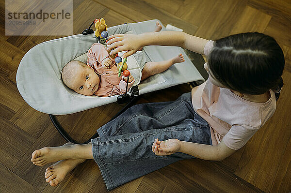 Girl playing with sister lying in baby bouncer at home