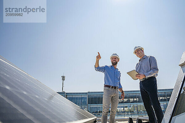 Two executives in safety gear discussing business on a rooftop adorned with solar panels