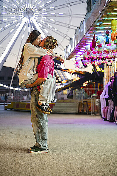 Boyfriend carrying girlfriend in arms at amusement park