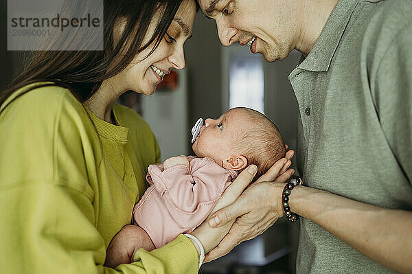 Mother and father carrying newborn baby sucking pacifier at home