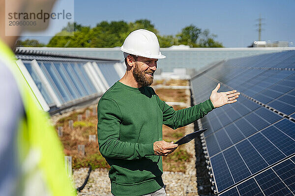 A man discusses business on a rooftop adorned with solar panels  using a tablet PC to communicate with a colleague