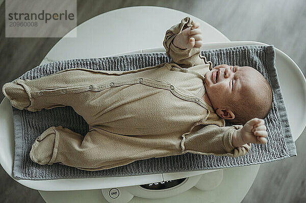 Crying baby lying on weighing scale at home