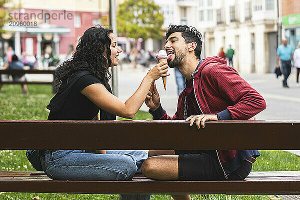 Smiling couple sitting on bench and eating ice cream in city