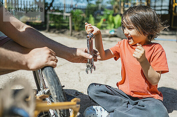 Happy boy sitting and giving wrenches to father in back yard