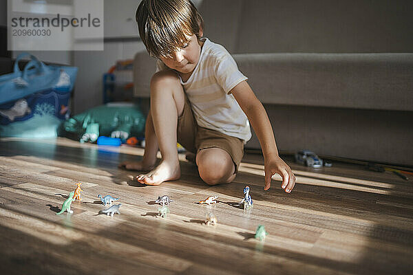 Boy sitting on floor and playing with dinosaur toys at home