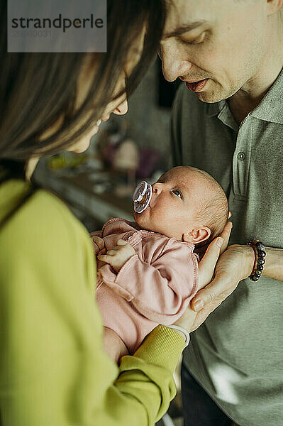 Parents carrying newborn baby girl sucking pacifier at home