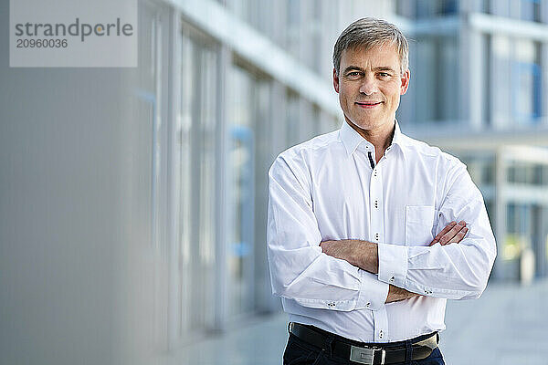 Casual businessman standing in front of office building with arms crossed