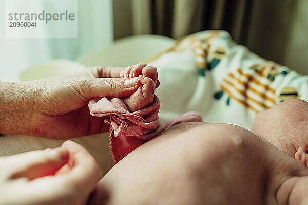 Mother holding newborn daughter's hand at home