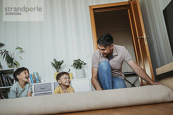 Playful father and sons rolling up carpet at home